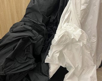 May include: A close-up of black and white fabric, possibly textiles or clothing. The black fabric is bunched and wrinkled, while the white fabric is smooth and flowing. The image suggests a focus on texture and contrast.