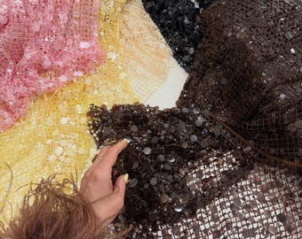May include: A collection of sequined fabric in various colors, including pink, yellow, beige, black, and brown. The fabrics are arranged in a layered display, showcasing the texture and sheen of the sequins. The image highlights the different colors and textures of the fabric.