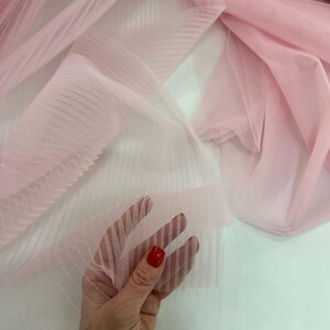 May include: Pink sheer fabric with vertical stripes. The fabric is pleated and has a soft, delicate texture.