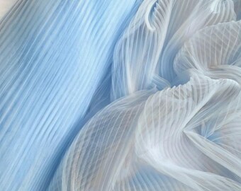 May include: A light blue fabric featuring a dense, vertical pleated texture. The material is semi-sheer and lightweight, with the pleats creating a series of parallel lines that run across the surface, adding depth and dimension to the textile.