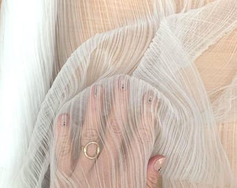 May include: Close-up of sheer white fabric with a textured, ribbed pattern. The fabric is held up, revealing the texture and translucence. The material appears lightweight and delicate, suitable for various craft projects or apparel.