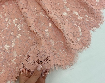 May include: Pink floral lace fabric with a scalloped edge. The lace has a delicate, intricate design.