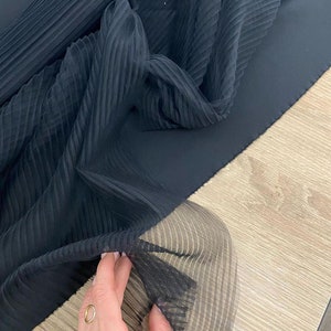 May include: Black pleated sheer fabric with a smooth, solid black fabric underneath. The sheer fabric is folded and draped over the solid fabric.