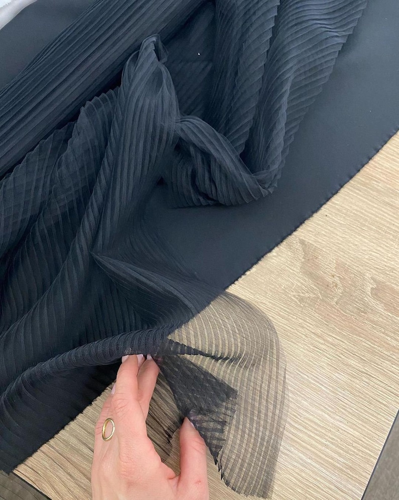 May include: Black pleated sheer fabric with a smooth, solid black fabric underneath. The sheer fabric is folded and draped over the solid fabric.