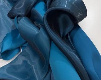 May include: An abstract composition of flowing fabric in shades of blue, from deep navy to vibrant turquoise. The material appears to be silk or a similar lightweight textile, with highlights and shadows creating a sense of depth and movement. The folds and curves of the fabric are prominent.