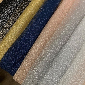 May include: Five rolls of sparkly tulle fabric in different colors: black, gold, navy blue, blush pink, and silver. The fabric has a subtle shimmer and is perfect for crafting and sewing projects.