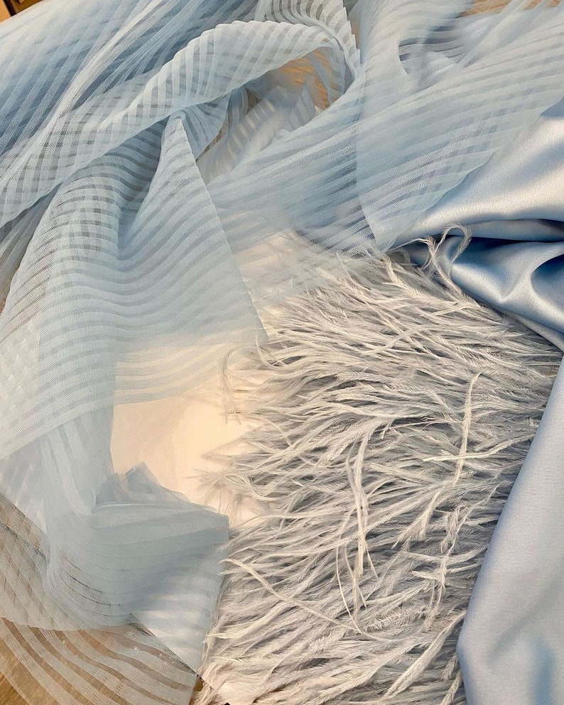 May include: A light blue fabric with a striped pattern and a layer of light blue feathers.