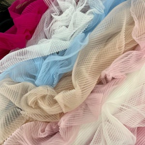 May include: A stack of pleated tulle fabric in various colors, including white, light blue, beige, pink, and fuchsia.