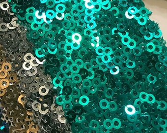 May include: Close-up of a fabric covered in teal sequins. The sequins are arranged in a random pattern and create a shimmering effect.