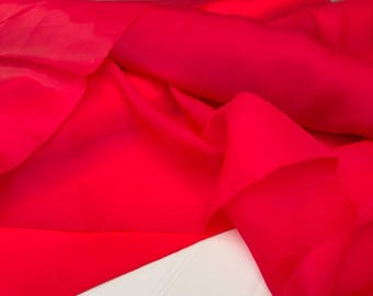 May include: Bright red fabric with soft folds and a flowing drape. The material appears to be a lightweight textile, possibly silk or a similar synthetic. The fabric is bunched up, creating shadows and highlights.