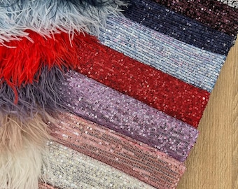 May include: A collection of fabric swatches featuring a variety of textures and colors. The swatches include a variety of feather trims and sequined fabrics in shades of red, pink, purple, blue, and white.