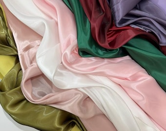 May include: A collection of flowing fabric in various colors, including white, pink, green, burgundy, and purple. The fabric has a shiny, silky texture, with folds and drapes creating a sense of movement and depth. The overall aesthetic is elegant and luxurious.
