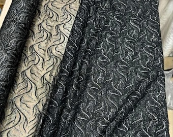 May include: Close-up of three rolls of fabric. The fabric on the left and right is black with a silver, swirling pattern. The fabric in the middle is a light beige with a black, swirling pattern. The fabric is likely used for clothing or home decor.