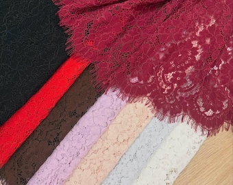 May include: A collection of colorful lace fabrics in various shades. The colors include black, red, brown, lavender, peach, light blue, and burgundy. The lace has a floral pattern and is arranged on a wooden surface.