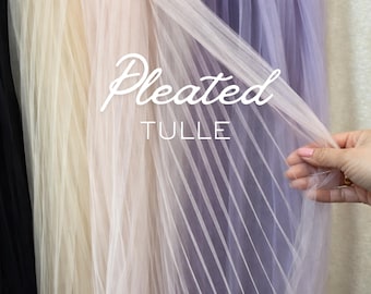 May include: Pleated tulle fabric in black, cream, and lavender. The sheer material is pleated and held by a hand. The text "Pleated Tulle" is displayed in a white script font.