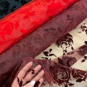Puede incluir: Tres rollos de tela transparente con un patrón de rosa de terciopelo. La tela está disponible en negro, rojo y burdeos.