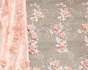 May include: Peach-colored floral lace fabric with 3D flowers. The lace has a delicate pattern of leaves and vines. The fabric is soft and sheer.
