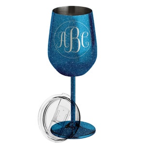 May include: A blue glitter wine glass with a silver rim and stem. The glass features a monogram in a circle. A clear lid is next to the glass. The stem and base are the same blue glitter material as the glass.