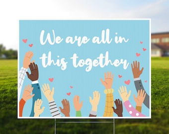 May include: A blue sign with the text "We are all in this together" in white.  The sign features a variety of hands reaching up in the air, with pink hearts scattered around them.