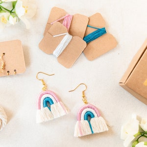 Può includere: Un kit per realizzare orecchini a nappina arcobaleno. Il kit include filo da ricamo bianco, rosa e blu, ganci per orecchini dorati e una scatola di cartone marrone con un design arcobaleno.