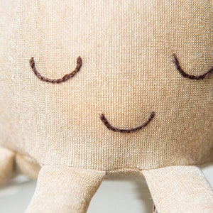 May include: A beige plush octopus with embroidered eyes and a smiling mouth.