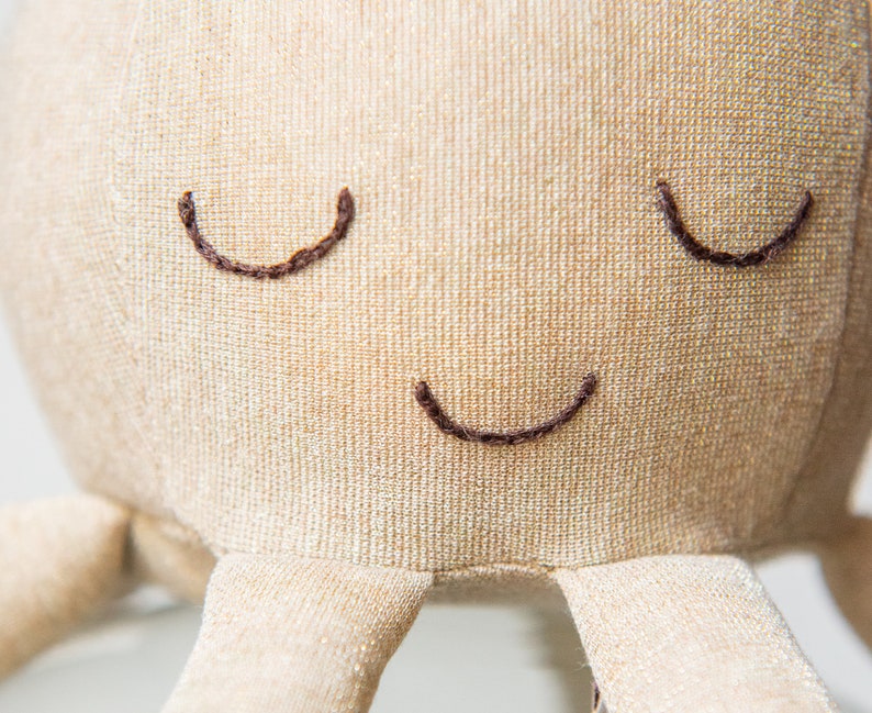 May include: A beige plush octopus with embroidered eyes and a smiling mouth.
