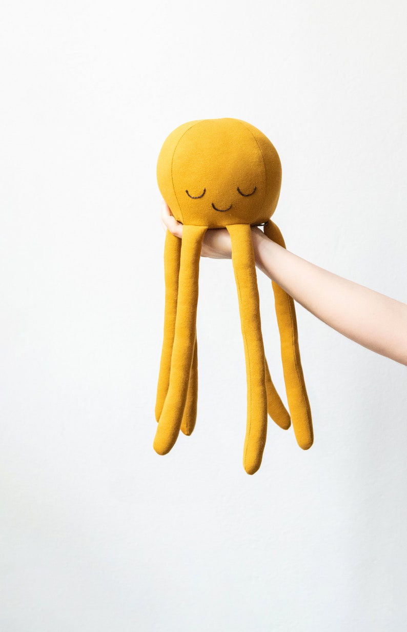 May include: A yellow plush octopus toy with a smiling face and closed eyes. The octopus has six long tentacles.