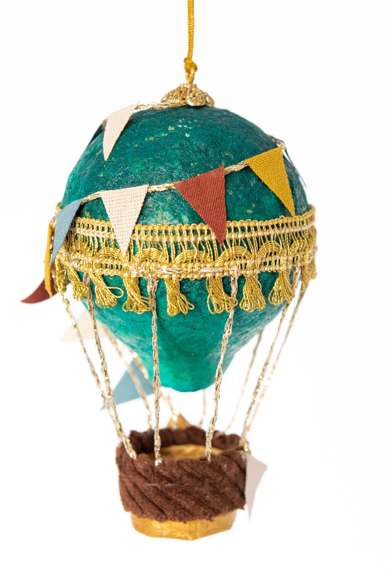 May include: A teal blue hot air balloon ornament with gold trim and colorful pennant flags. The balloon has a brown fabric basket and gold strings.