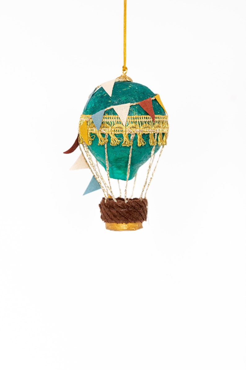 May include: A teal blue hot air balloon ornament with a gold trim and brown basket. The balloon is decorated with colorful paper flags.
