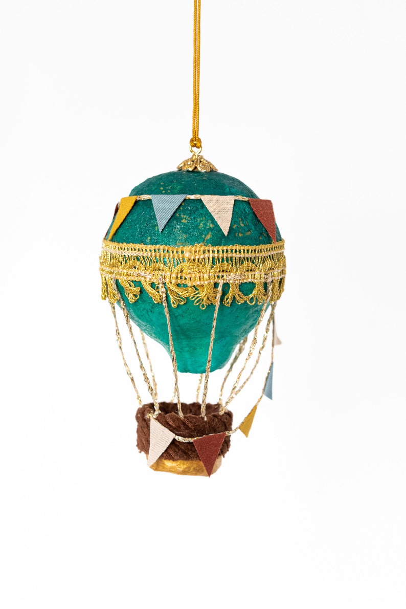 May include: A teal blue hot air balloon ornament with gold trim and brown fabric basket. The balloon is decorated with colorful pennants.