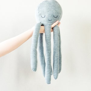 May include: A grey plush octopus toy with a smiling face and closed eyes. The octopus has five long tentacles.