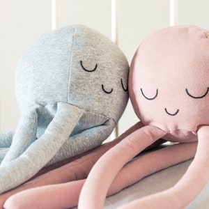 May include: Two plush octopus toys with embroidered eyes and smiles. One octopus is grey and the other is pink.