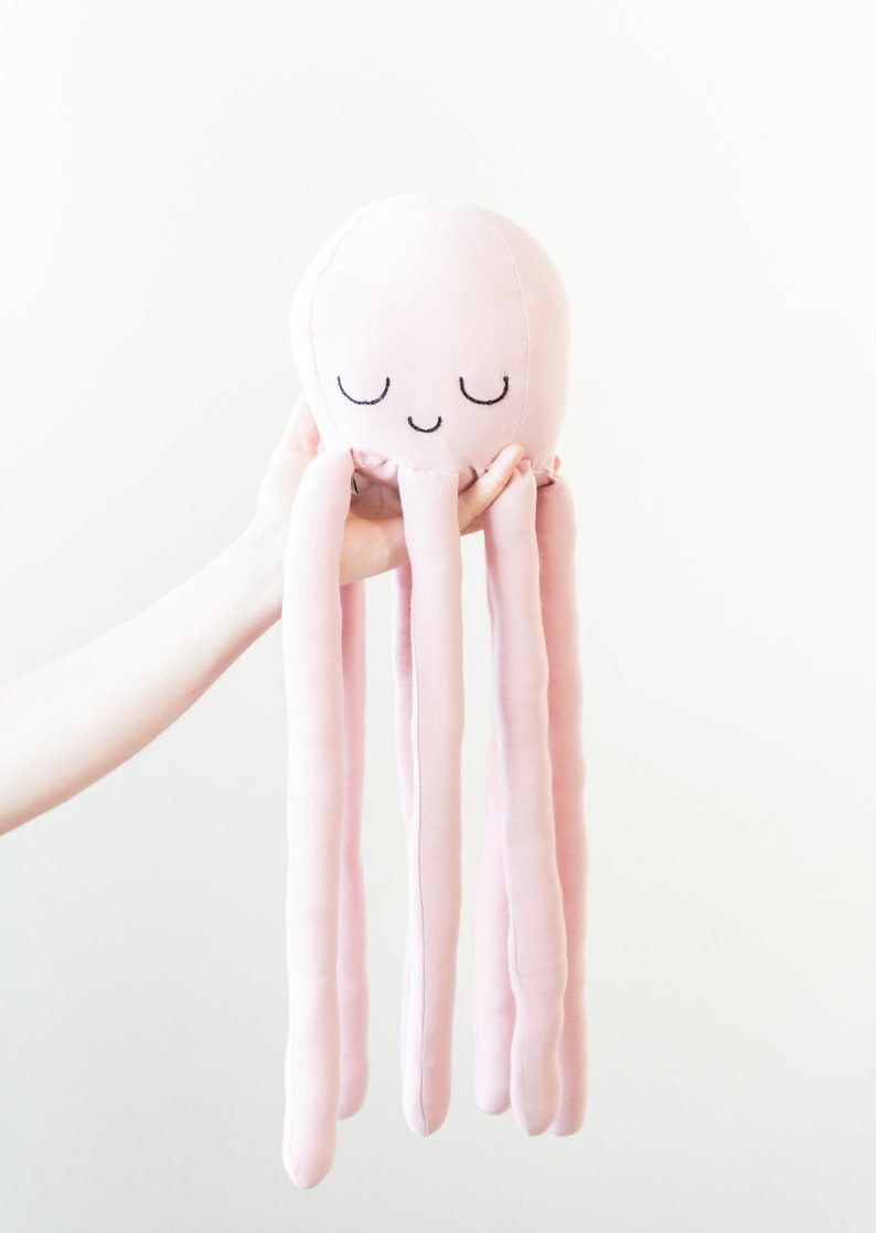 May include: A pink plush octopus with embroidered eyes and a smiling mouth. The octopus has long, thin tentacles.
