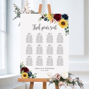 May include: A white wedding seating chart with a floral design featuring sunflowers, burgundy roses, and eucalyptus leaves. The chart is titled "Find your seat" and lists the names of guests assigned to each table. The bottom of the chart reads "Amelia & Jonathan 10.12.2023".
