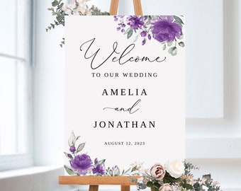 May include: A white wedding welcome sign with purple and green watercolour flowers. The sign reads "Welcome to our wedding Amelia and Jonathan August 12, 2023".