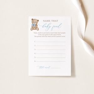 May include: A printable baby shower game card featuring a brown teddy bear illustration and the text "NAME THAT baby food". The card instructs players to taste, smell, or look at each baby food sample and write their guess in the space provided. The person with the most correct answers wins.