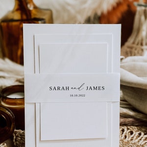 May include: A white wedding invitation with a simple design. The invitation has three layers and a band with the text "SARAH and JAMES 10.10.2022".