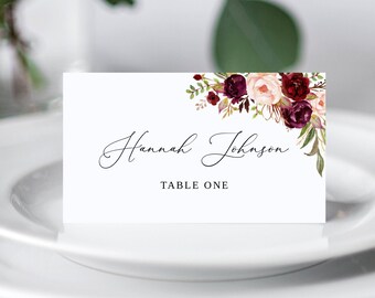 May include: White place card with a burgundy and blush floral design. The text reads "Hannah Johnson" and "Table One".