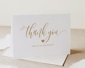 Puede incluir: Una tarjeta de agradecimiento blanca con letras doradas que dice "gracias" con un pequeño corazón dorado y los nombres "Emilia & Jonathan" impresos debajo.