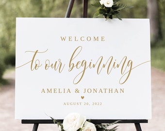 May include: White wedding welcome sign with gold lettering that reads "Welcome to our beginning Amelia & Jonathan August 20, 2022". The sign is on a black easel with white flowers.