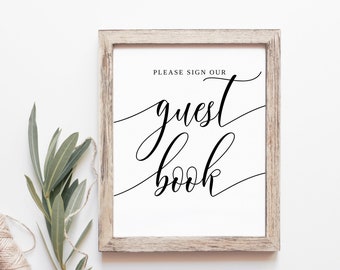 May include: A white sign with a black wooden frame and the text "PLEASE SIGN OUR guest book" in a cursive font.