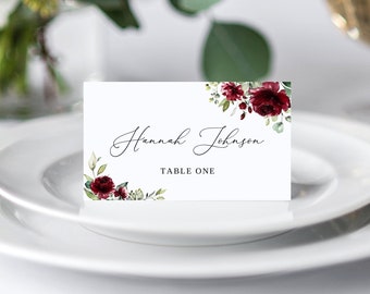 May include: White place card with a burgundy floral design and the text "Hannah Johnson" and "Table One".