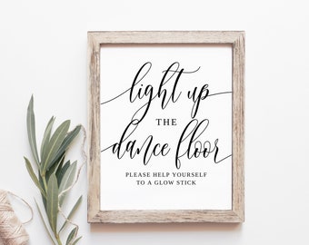 May include: A white sign with a wooden frame, featuring the text "light up the dance floor" in black cursive script. Below the text, it reads "Please help yourself to a glow stick."