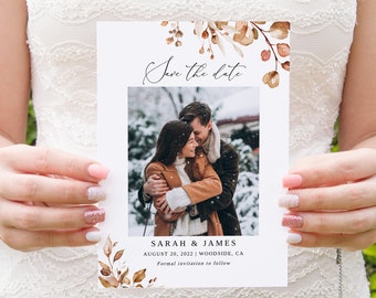 May include: Save the date card with a photo of a couple in a snowy setting. The card features a watercolor floral design in shades of brown and beige. The text reads "Save the date", "Sarah & James", "August 20, 2022 | Woodside, CA", and "Formal invitation to follow".