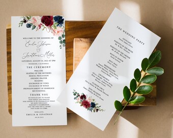 May include: Wedding ceremony program with a floral design featuring burgundy, pink, and blue flowers. The program lists the officiant, parents of the bride and groom, maid of honor, best man, bridesmaids, groomsmen, flower girls, and ring bearers.
