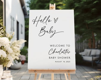 Pode incluir: Um cartaz de boas-vindas branco com texto em caligrafia preta que diz "Hello Baby" com um símbolo de coração. O cartaz também diz "Bem-vindo ao Chuveiro de Bebê da Charlotte em 16 de agosto de 2025".