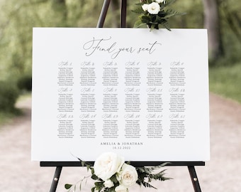 May include: A white wedding seating chart with black text on an easel. The chart is titled "Find your seat" and lists guests by table number. The bottom of the chart reads "Amelia & Jonathan 10.12.2022".