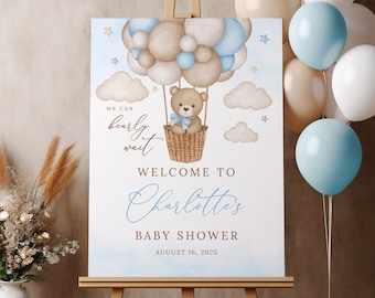 Peut inclure: Une pancarte de bienvenue pour une fête prénatale bleue et marron avec un ours en peluche dans un ballon à air chaud fait de ballons. La pancarte indique "We can barely wait" et "Welcome to Charlotte's Baby Shower August 16, 2025".