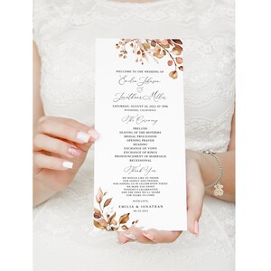 May include: Wedding ceremony program with a watercolor floral design in shades of brown and beige. The program lists the order of events for the wedding of Emilia and Jonathan on August 20, 2022, in Woodside, California.