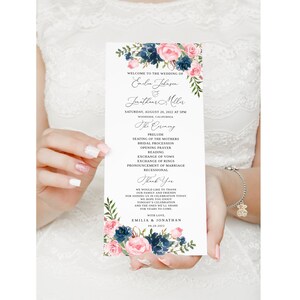 Könnte beinhalten: Hochzeitszeremonie-Programmkarte mit einem floralen Design mit rosa und blauen Blumen. Die Karte listet die Reihenfolge der Zeremonie auf, einschließlich des Präludiums, des Platznehmens der Mütter, des Hochzeitszuges, des Eröffnungsgebets, der Lesung, des Austauschs der Gelübde, des Austauschs der Ringe, der Bekanntgabe der Ehe und des Auszugs. Die Karte enthält auch das Datum und den Ort der Hochzeit sowie die Namen der Braut und des Bräutigams: Emilie Johnson und Jonathan Miller.